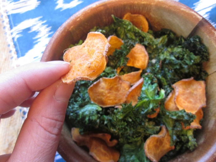 kale and sweet potato chips in a wooden bowl woman holding a piece