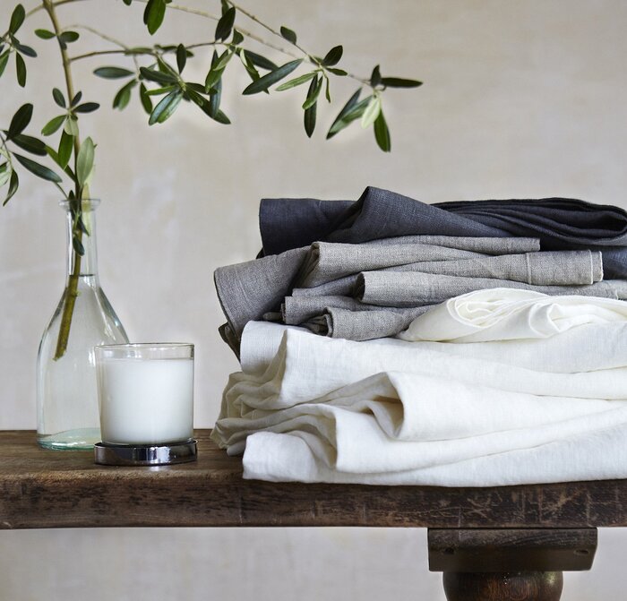 white and grey linen towels on a dark wooden table with a white candle and a branch in a vase