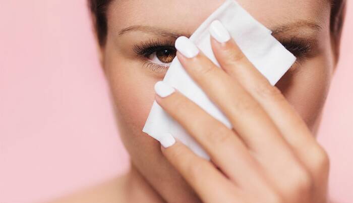 woman with white nail polish using a white wet wipe to take her makeup off