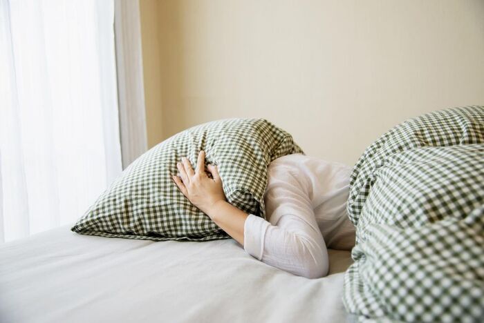 daily habits sleep person lying in bed with their pillow on their had not wanting to wake up