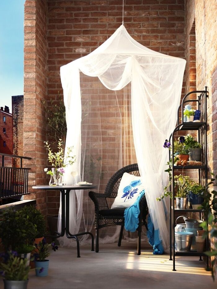 mosquito net in a small balcony over a chair and a small round table with brick walls around