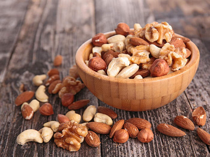 Variety of nuts in a small wooden bowl on a dark wooden table
