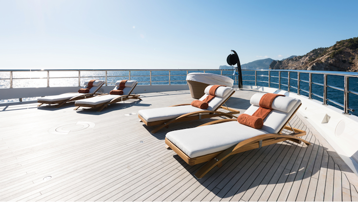 modern yacht deck with white lounge chairs and a rocky coast in the background