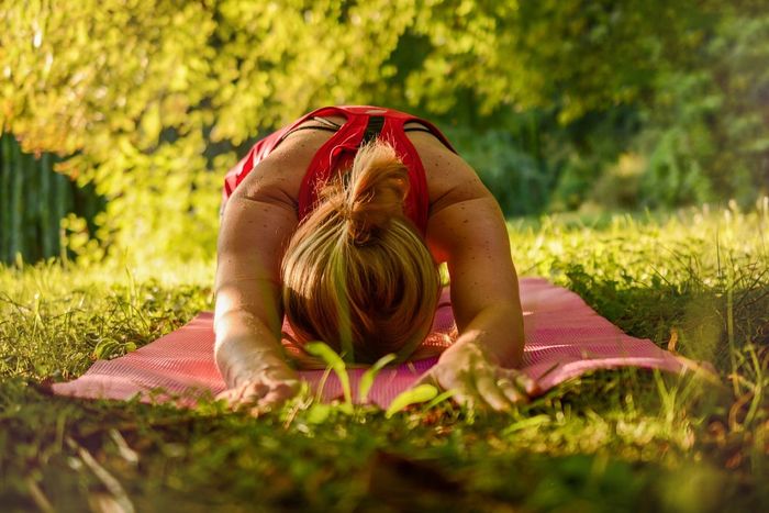 outdoor yoga pose woman doing yoga in the garden on a pink yoga mat bowing down