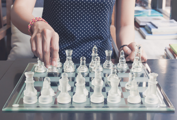 playing chess daily habits woman in a dark blue dotted dress playing chess with transparent figurines