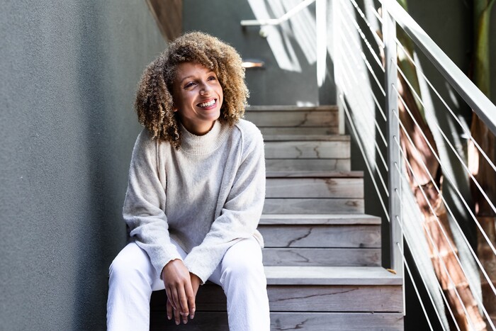 prioritize time woman in comfortable clothes sitting on a staircase smiling with curly hair