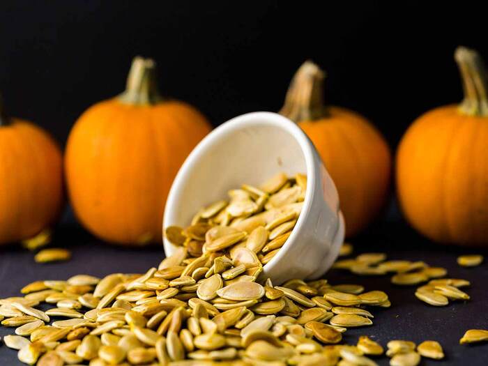 pumpkin seeds spilling from a white team cup with orange pumpkins in the background