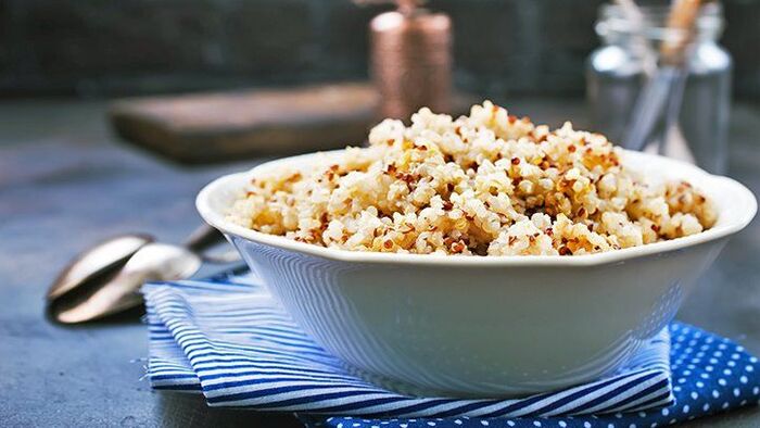 bowl with quinoa on a blue towel on a table with a spoon next to it and other kitchen ware in the background