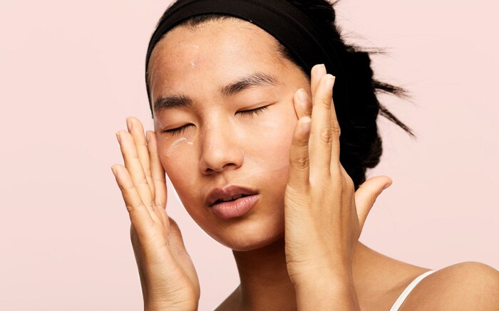 retinol face asian woman with her hair up applying cream on her face and under her eyes