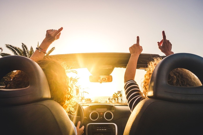 road trip pandemic summer two people in a cabrio car roof down at sunset with hands up in the air