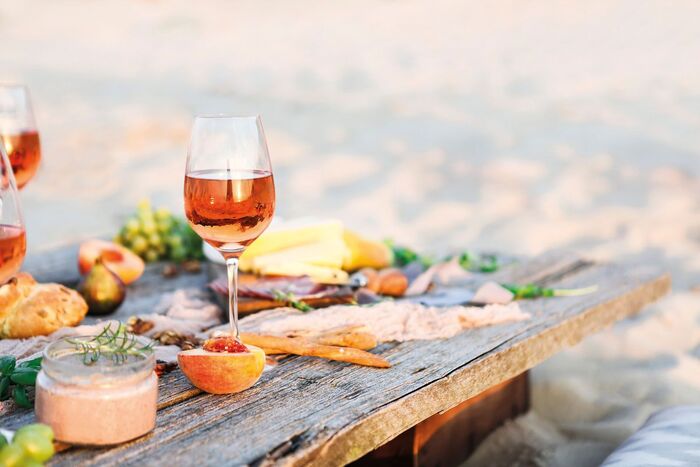 rose wine served on a wooden table on the beach with different snacks 