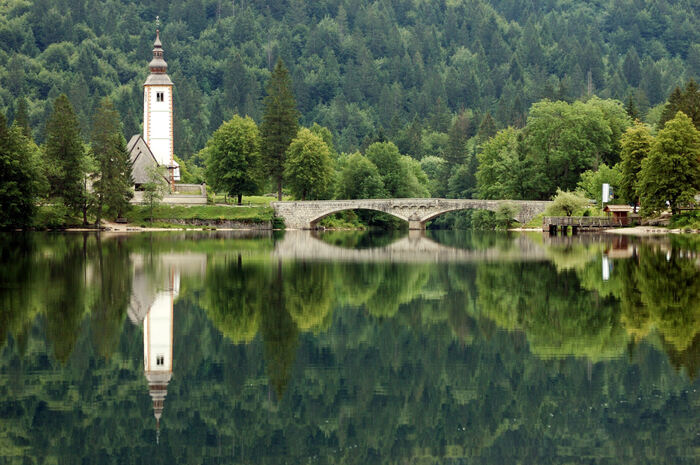 slovenia lake bohinj with a stone bridge and a white tower surrounded by forests