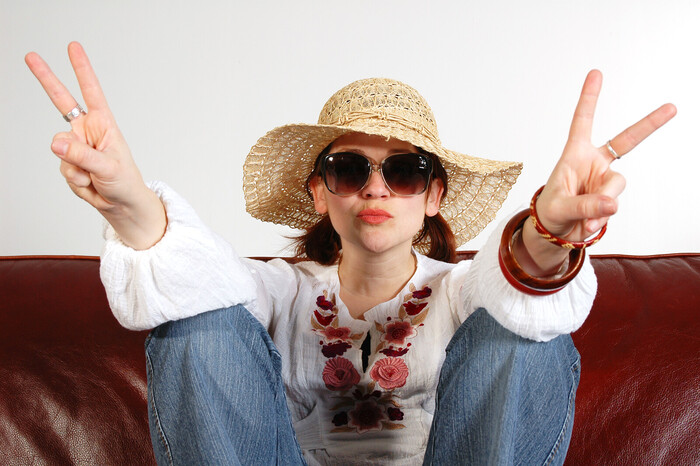 pandemic summer woman with a sun hat and sunglasses in jeans sitting on a coach with two hands up in a peace sign