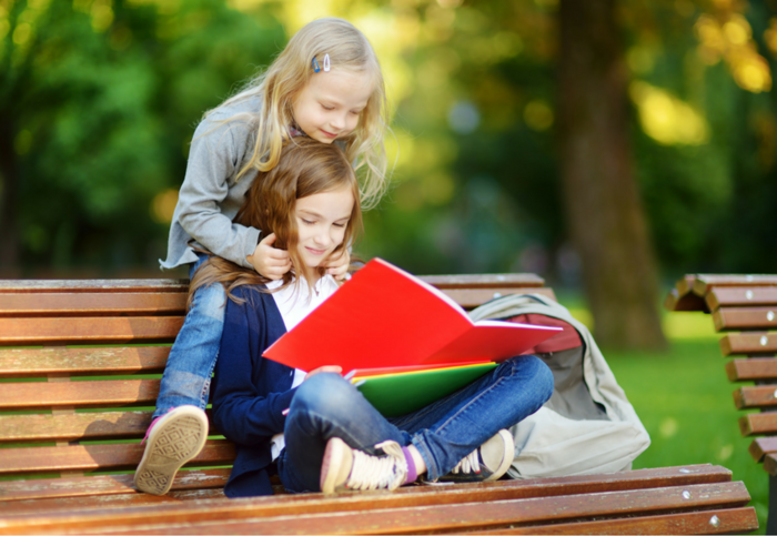 summer study two girls on a bench reading a large red notebook