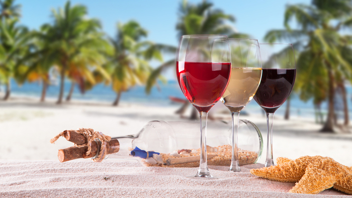 Summer wines three glasses of different wine on the beach next to a bottle with palm trees in the background