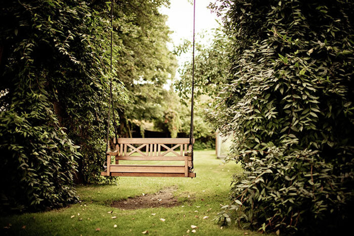 swing bench in a green garden with bushes and trees on both sides