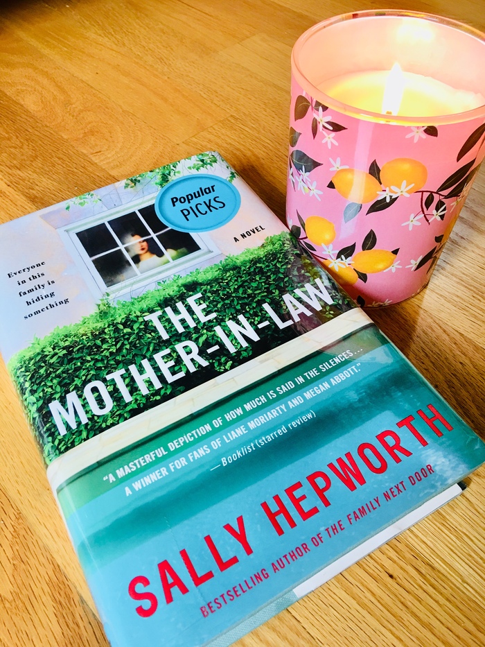 the mother in law book lying on a wooden table with a candle burning next to it