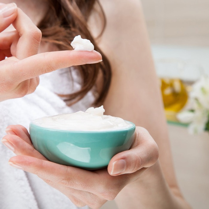 vitamin A cream woman in a bath towel taking white cream with her finger from a light blue bowl