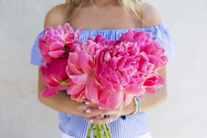 woman in light blue off shoulder top holding bright pink peonies 