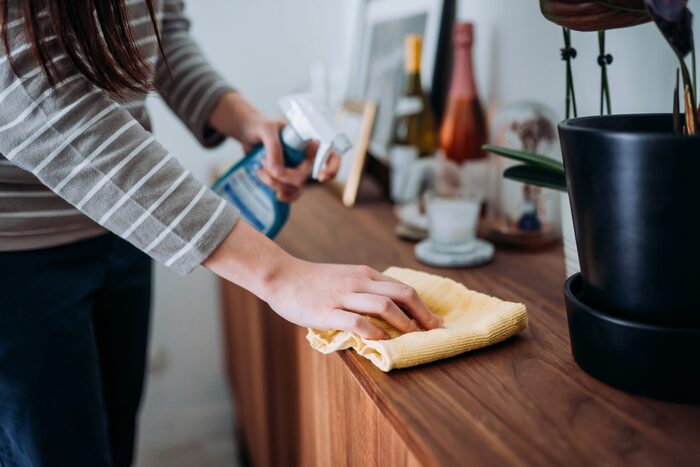 woman cleaning the dust at home with a cleaning spray on a wooden surface