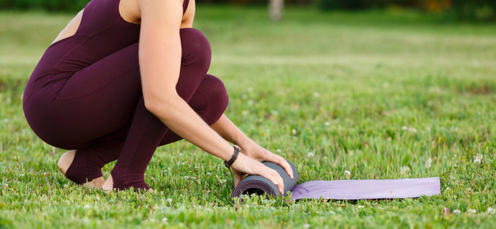 close-up of a woman in black sports clothes rolling out a yoga mat on the green grass