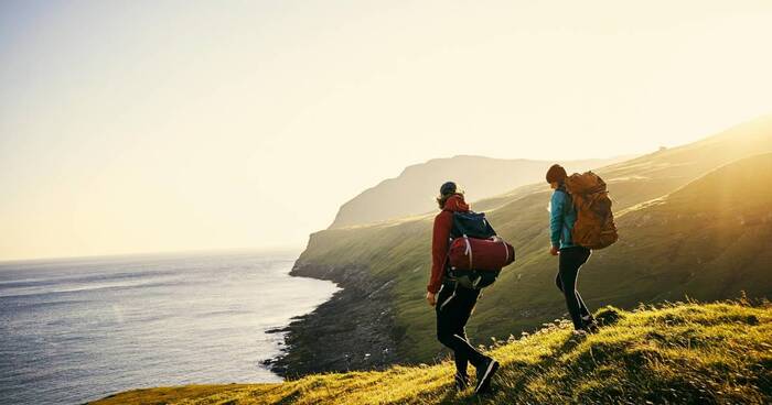 active vacations for couples couple hiking on grassy cliffs with the sea in the background