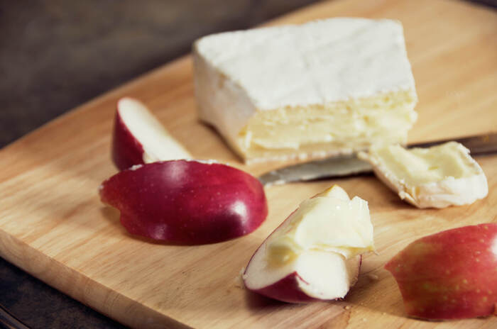 red apple slices and brie cheese on a wooden cutting board with a knife