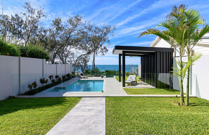Modern green yard with short grass blue sky and a pool with a black hut 