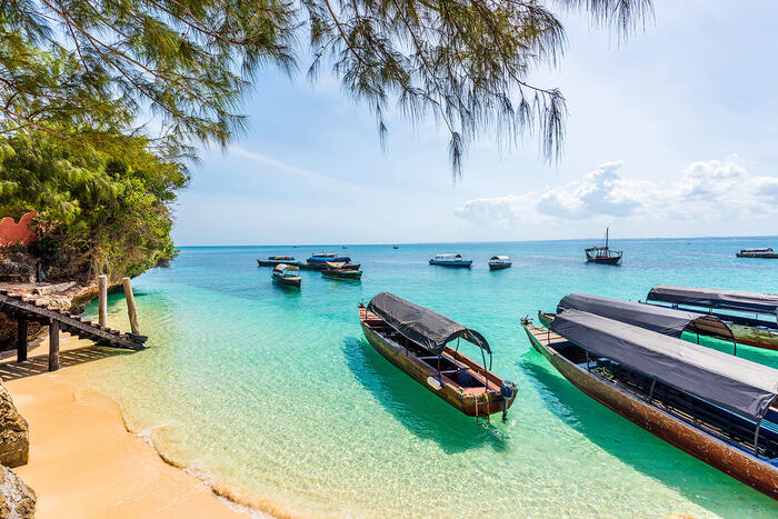 beach on madagaskar with crystal blue water and wooden boats floating on it