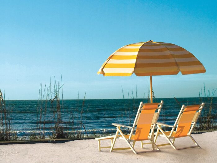 beach set up with two yellow chairs and a large white and yellow parasol overlooking the sea