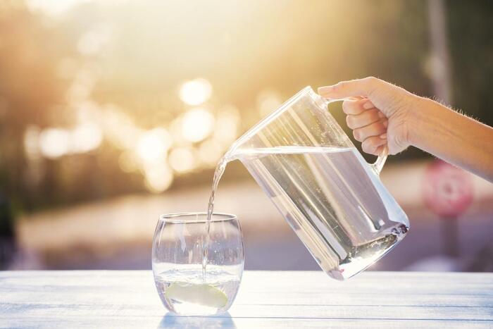 benefits of mineral water female hand pouring water from a large jug into a glass