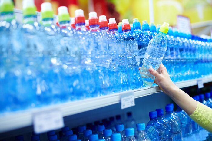 bottled water hand picking a bottle of water from the supermarket large shelf full of bottled water with colorful caps