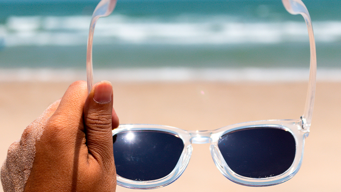choose sunglasses hand holding a pair of white sunglasses with dark glass with the sea in the background
