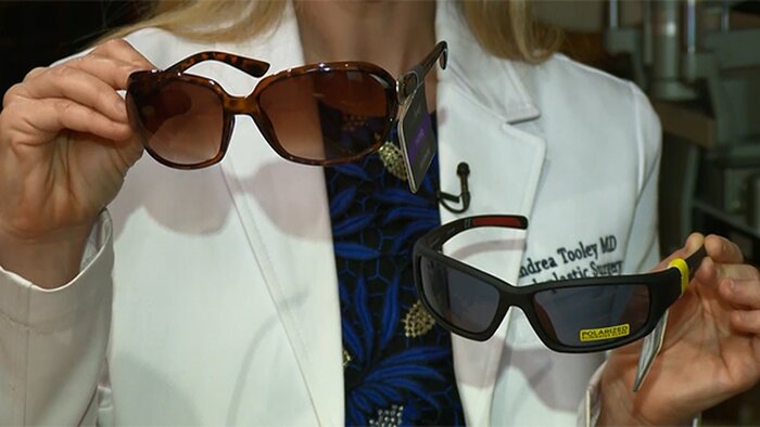 choosing between sunglasses woman in white coat demonstrating two pairs of sunglasses one sports and one elegant