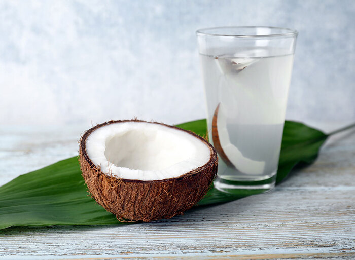 coconut water and half a coconut on a green leaf and grey table