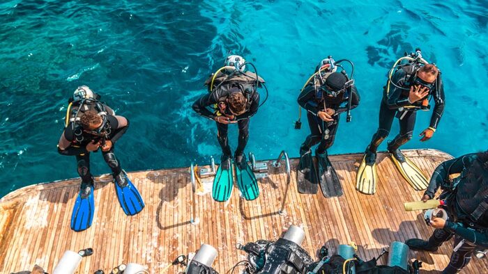 four divers ready and equipped to jump into the water from a deck