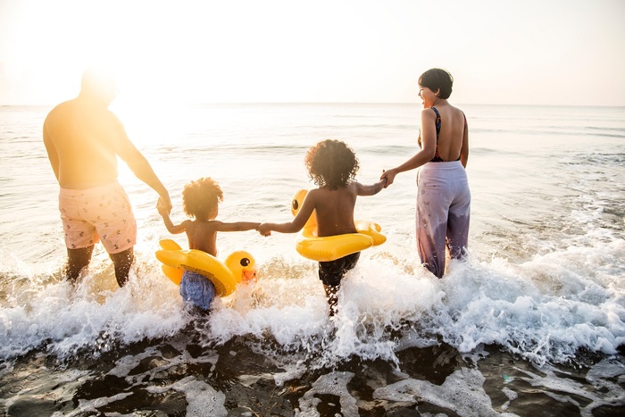 black family of four in swim suits entering the sea at sunrise white waves around them