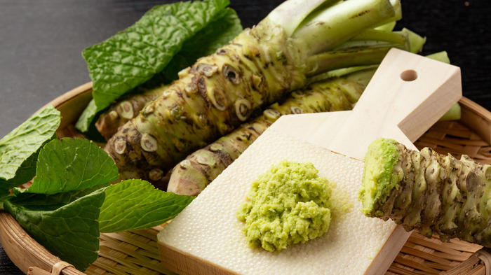 grated wasabi on a little wooden board wasabi roots in a basket with green wasabi leaves