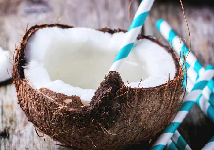 half coconut with a white and blue straw thick coconut milk inside