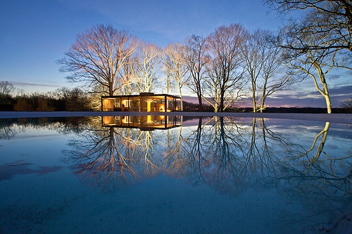 lake property at night glass structure surrounded by trees and a large pool of water