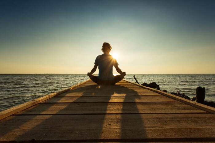 man meditating on sea alley right next to the water at sunset