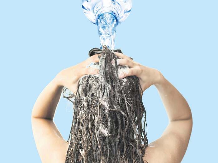 mineral water for hair woman washing her hair with shampoo and bottle of mineral water pouring on her head