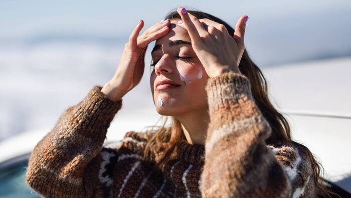 mountain sunscreen woman in a sweater applying sunscreen on her face with both her hands