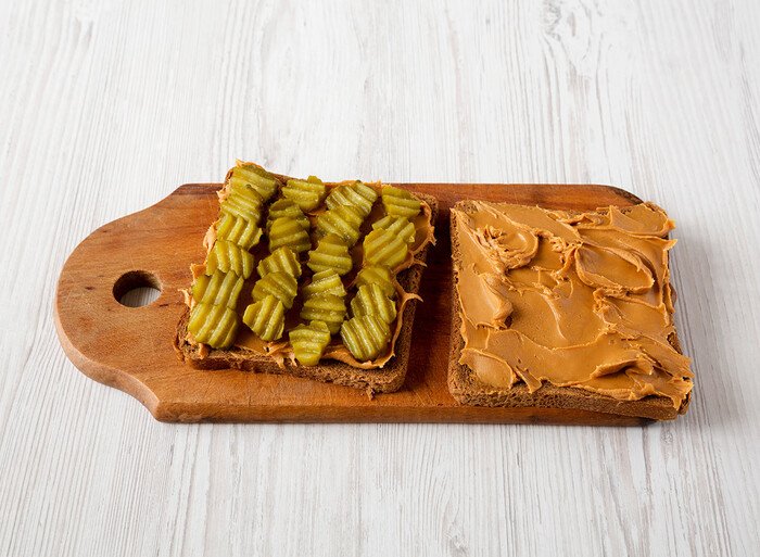 peanut butter and pickle sandwich on a wooden cutting board on a white wooden table