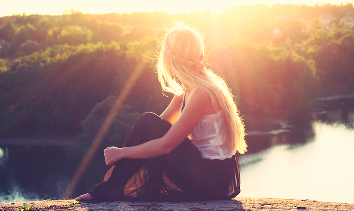 relax your mind woman with long blond hair sitting near the water looking at the sun raising and nature 