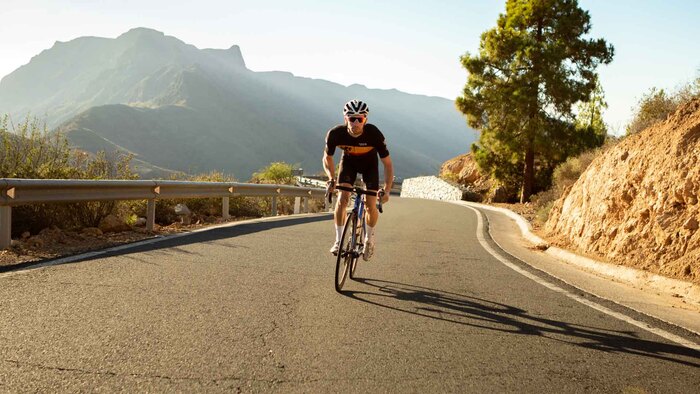 road cycling man on his bicycle cycling up a hill with cliffs in the background