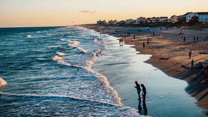 people walking along a wide beach at sunset with soft waves on the beach