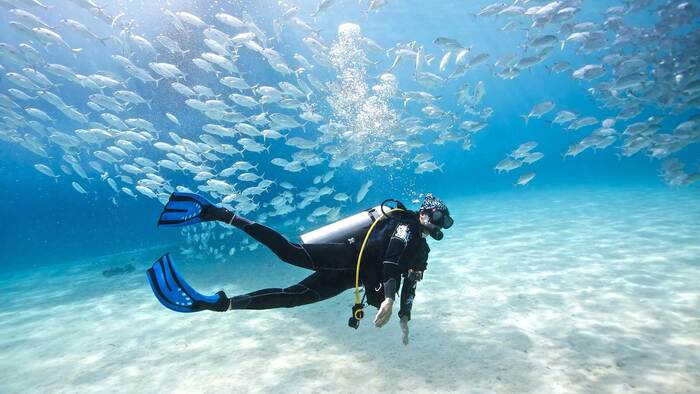 scuba diver in the maldives with a lot of little silver fish around him almost reaching the sandy bottom