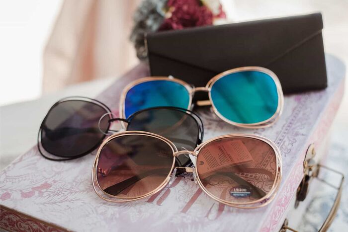 several pairs of sunglasses in different colors on a little decorative suitcase with a dark pouch in the background