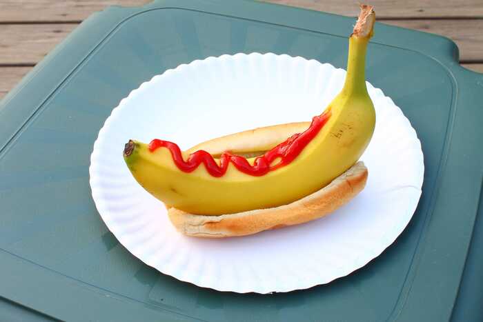strange food combos banana hot dog on a white plate with bread and ketchup on the banana